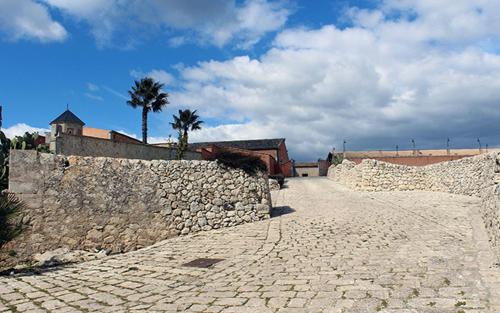 a stone wall with a palm tree and a building at Feudo Bauly in Palazzolo Acreide