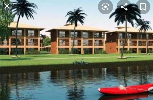 a building with palm trees and a red boat in the water at Villa das Águas - Térreo frente lago in Estância