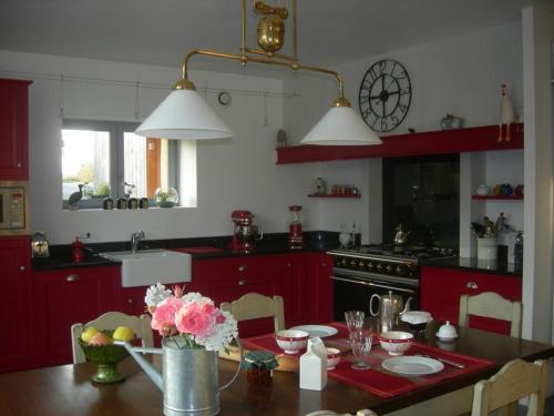 eine Küche mit roten Schränken und einem Tisch mit Blumen darauf in der Unterkunft Chambres d'hôtes La Penhatière in Baulon