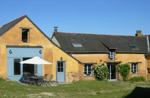 a yellow house with a table and an umbrella at Chambres d'hôtes La Penhatière in Baulon