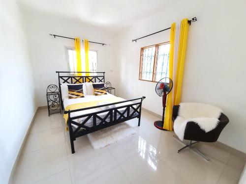 - une chambre avec un lit avec des rideaux jaunes et une chaise dans l'établissement APPARTEMENT MAKEPE BM 2, à Douala