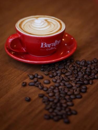 a cup of coffee on a red plate with coffee beans at Baratha Hotel & Resto in Bondowoso