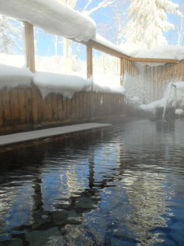 a swimming pool covered in snow next to a fence at K's House Hokkaido - Asahidake Onsen Hostel in Higashikawa