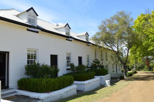 an old white house with bushes and trees at Lythgo's Row Colonial Cottages in Pontville