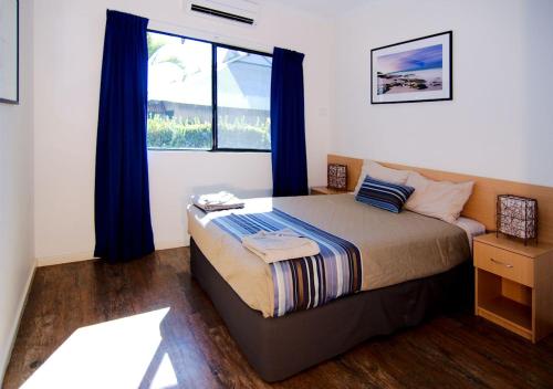 a bedroom with a bed, a desk, and a window at Cable Beach Apartments in Broome
