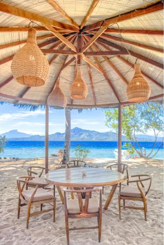 a table and chairs under a straw umbrella on the beach at Kuda Laut Boutique Dive Resort in Bunaken