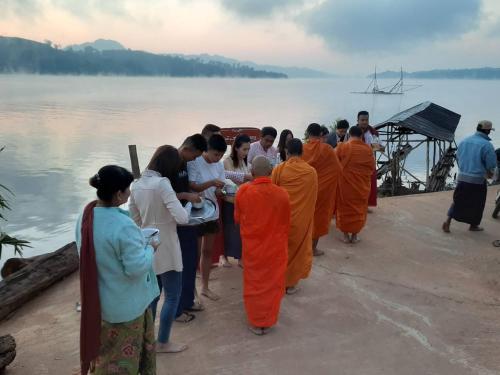 a group of people in orange robes standing on a dock at Baan Dongsak River view in Sangkhla Buri
