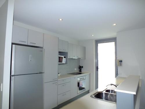 a white kitchen with a refrigerator and a sink at Pacific Marina Apartments in Coffs Harbour
