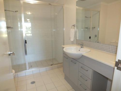 a white bathroom with a shower and a sink at Pacific Marina Apartments in Coffs Harbour
