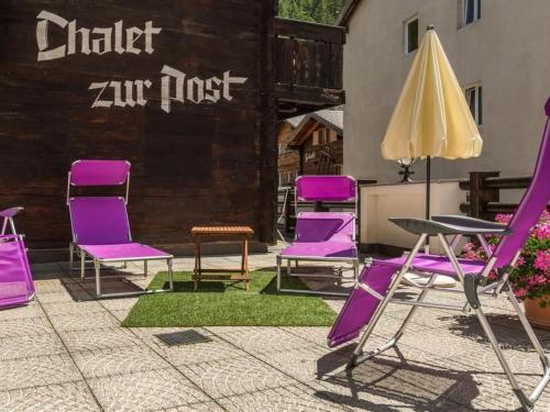 un gruppo di sedie viola, un tavolo e un ombrellone di Apartment Zur Post by Interhome a Saas-Almagell