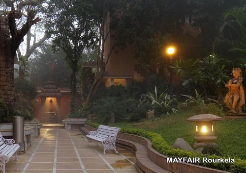 a garden with two white benches and a street light at Mayfair Rourkela in Panposh