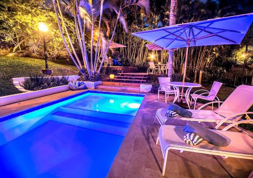 a swimming pool with chairs and a table and an umbrella at Pousada Morada dos Bougainvilles in Praia do Rosa