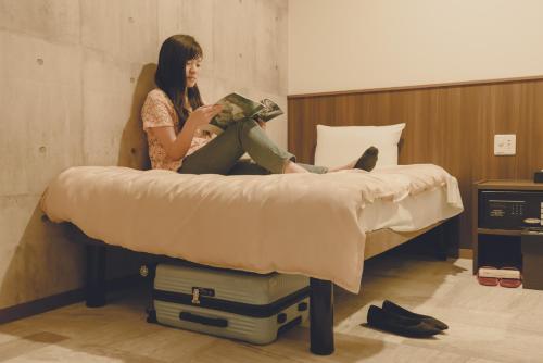 Kobieta siedząca na łóżku czytająca książkę w obiekcie Grand Cabin Hotel Naha Oroku for Men / Vacation STAY 62323 w mieście Naha