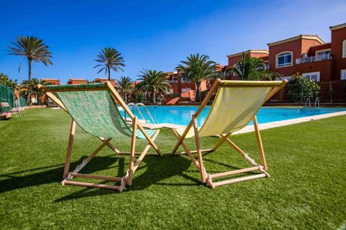 2 chaises assises sur l'herbe près d'une piscine dans l'établissement Home FTV, by Comfortable Luxury, à Corralejo