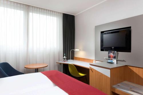 a hotel room with a bed and a desk with a television at Ramada by Wyndham Hannover Messe in Hannover