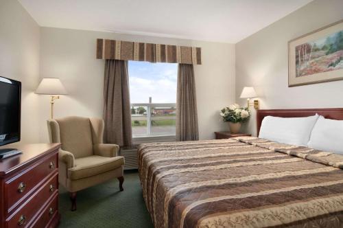 um quarto de hotel com uma cama e uma cadeira e uma janela em Travelodge by Wyndham Stony Plain em Stony Plain