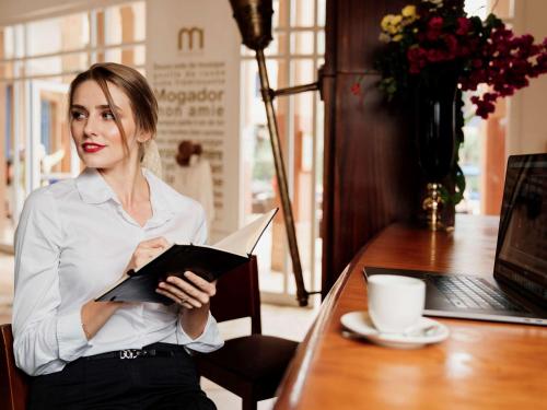 a woman sitting at a table holding a book at Le Médina Essaouira Thalassa Sea & Spa - MGallery Collection in Essaouira