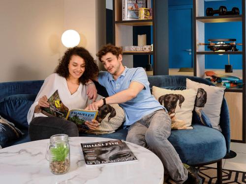 a man and woman sitting on a couch reading a book at Aparthotel Adagio Monaco Monte Cristo in Beausoleil