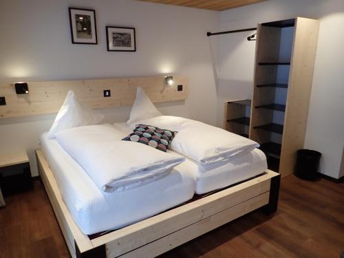 uma cama grande com lençóis brancos e almofadas em Hotel Furka em Oberwald