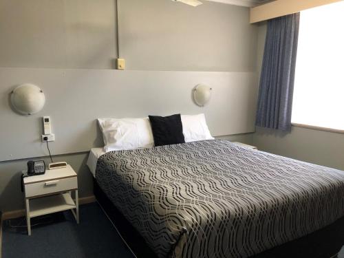 Flinders Motel في ولونغونغ: غرفة نوم بسرير وموقف ليلي مع هاتف