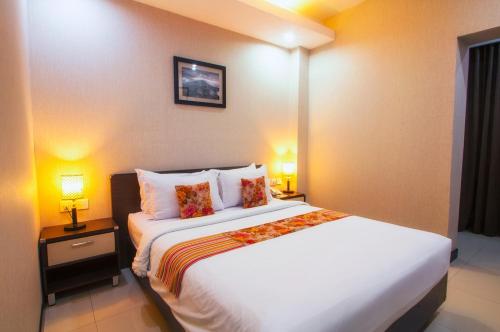a bedroom with a large white bed with two lamps at Daima Hotel Padang in Padang