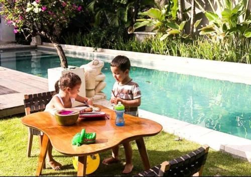 two children sitting at a table next to a pool at Chandra Bali Villas in Seminyak