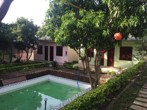 a swimming pool in front of a house with a tree at Nhà Nghỉ THẢO NGUYÊN XANH in Buon Ma Thuot