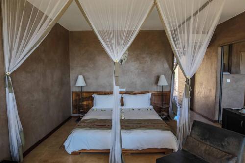 Schlafzimmer mit einem Bett mit weißer Bettwäsche und Vorhängen in der Unterkunft Isalo Rock Lodge in Ranohira