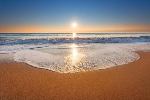 a beach with the sun rising over the ocean at Ramada Hotel & Suites by Wyndham Ajman in Ajman 