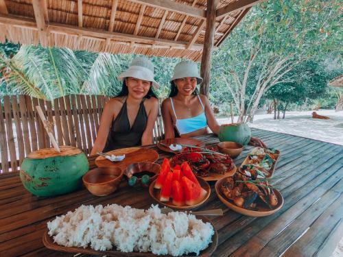 twee vrouwen aan een tafel met eten erop bij Cocovana Beach Resort in Busuanga