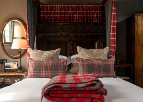 a bedroom with a bed with red and green plaid pillows at The Lygon Arms - an Iconic Luxury Hotel in Broadway