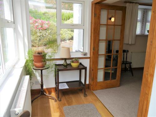 Habitación con ventanas y mesa con macetas. en Rowan Cottage en New Galloway