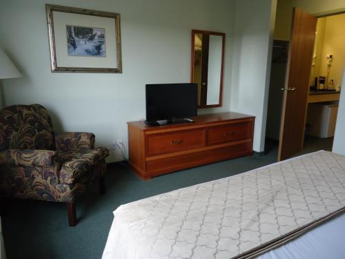 a bedroom with a bed and a tv and a chair at Super 8 by Wyndham Dauphin in Dauphin