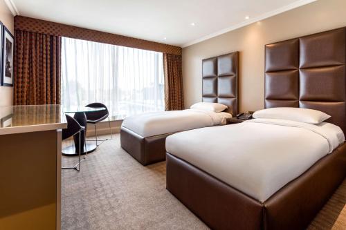a hotel room with two beds and a desk at Radisson Blu Hotel & Conference Centre, London Heathrow in Hillingdon