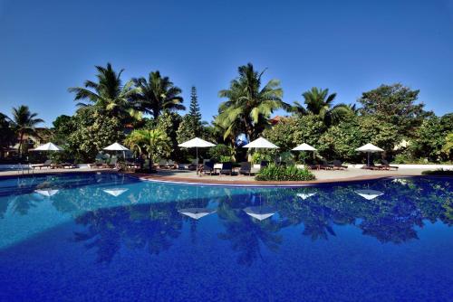 a large swimming pool with umbrellas and palm trees at Radisson Blu Resort, Goa in Cavelossim