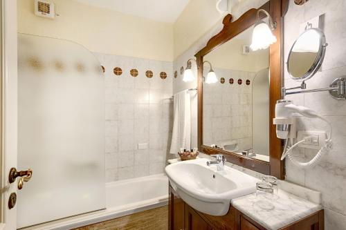 فندق جراند سميرالدو بيتش في بايا سردينيا: حمام مع حوض ومرآة وحوض استحمام