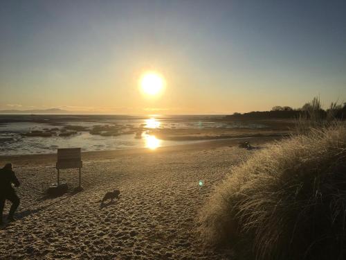 a person standing on a beach at sunset at STUNNING LODGE - HOME FROM HOME Kippford, Dalbeattie in Dalbeattie