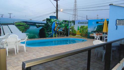 a patio with a swimming pool with white chairs and a mural at Visk Palace Hotel e Restaurante in Foz do Iguaçu
