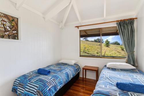two beds in a room with a window at Alstonville Country Cottages in Alstonville