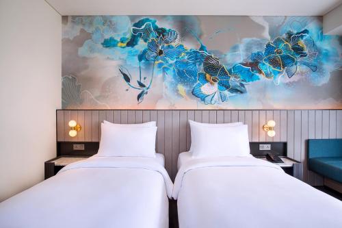 two beds in a room with a painting on the wall at Mercure Bengkulu in Bengkulu