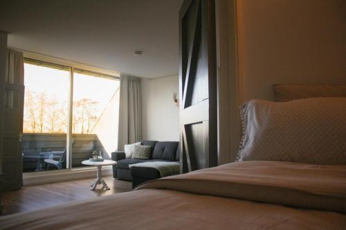 een slaapkamer met een bed, een bank en een raam bij T'hûs bed & breakfast in Katlijk