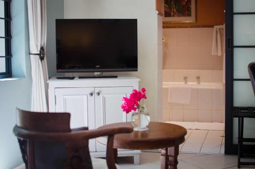 a living room with a television and a table with a vase of flowers at Paradiso Guesthouse & Self-catering Cottage in Cape Town