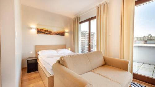 a bedroom with a bed and a couch and a window at VacationClub – Platan 2E Apartament 19 in Świnoujście