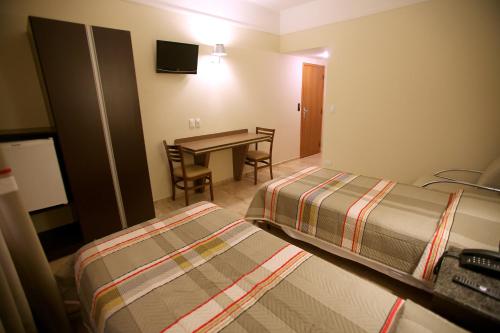 a hotel room with two beds and a desk and a table at Soneca Plaza Hotel in Sao Paulo