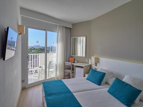 a bedroom with a bed with blue pillows and a balcony at BQ Delfín Azul Hotel in Port d'Alcudia