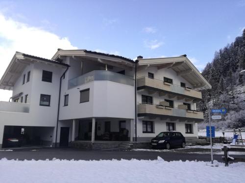 un gran edificio blanco con un coche aparcado en la nieve en Gästehaus Holaus, en Mayrhofen