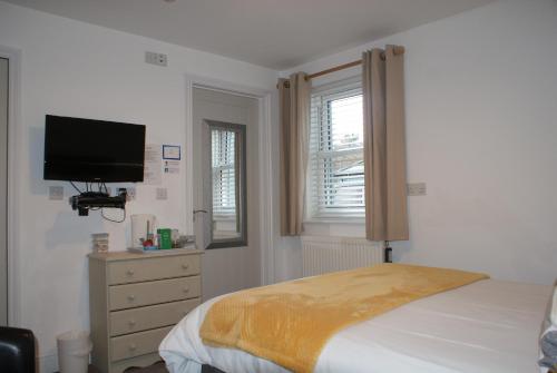 a bedroom with a bed and a tv and a dresser at Tirah Guest House in Aldeburgh