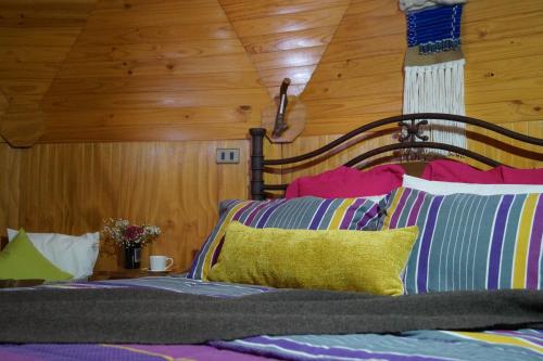 a bed with colorful pillows and a wooden ceiling at Cabañas Domos May-Ling in La Ensenada