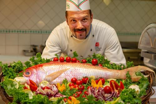 a chef in a kitchen with a fish on a table at Hotel Caesar Palace in Giardini Naxos