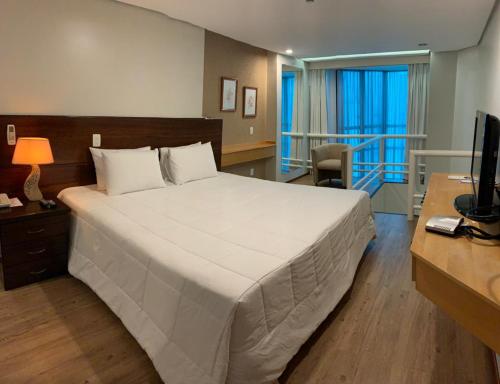 Schlafzimmer mit einem großen weißen Bett und einem Schreibtisch in der Unterkunft Bahamas Suíte Hotel in Campo Grande